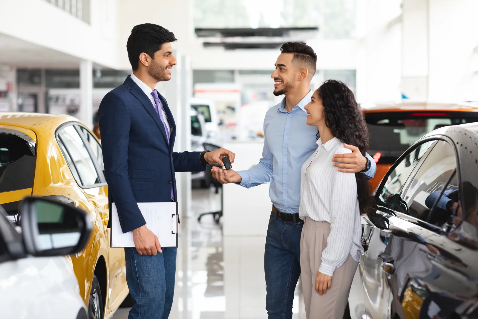Sales associate handing keys to a couple in a high ticket showroom